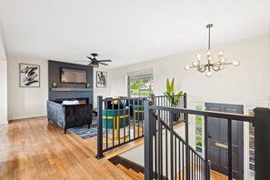 A spacious living area with a modern fireplace, a ceiling fan, and a staircase leading to an upper level. - Group Getaway- Theater Room + Game Room (Forest Park)