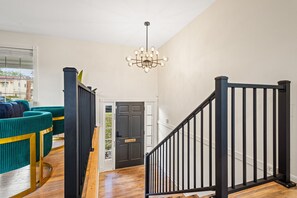 A staircase with black railings leading to a door, a chandelier, and teal upholstered chairs. - Group Getaway- Theater Room + Game Room (Forest Park)