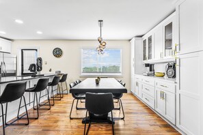 A modern kitchen with a dining table, chairs, and a large window with blinds. - Group Getaway- Theater Room + Game Room (Forest Park)