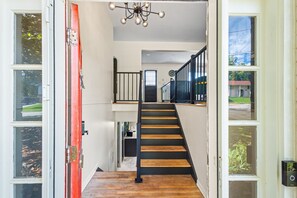 A staircase leading to a second floor with a black railing, a red door, and a ceiling light fixture. - Group Getaway- Theater Room + Game Room (Forest Park)