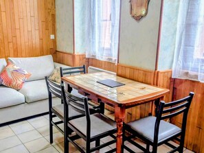 A dining area with a wooden table and chairs, a sofa with cushions, and a window with curtains. - Studio mountain view - 4 guests (Cauterets)