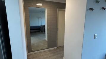 A hallway with a wooden floor, a mirror, and a door leading to a bedroom with a bed and a nightstand.