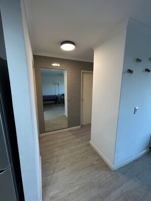 Ein Flur mit Holzboden, einem Spiegel und einer Tür zu einem Schlafzimmer mit Bett und Nachttisch.
