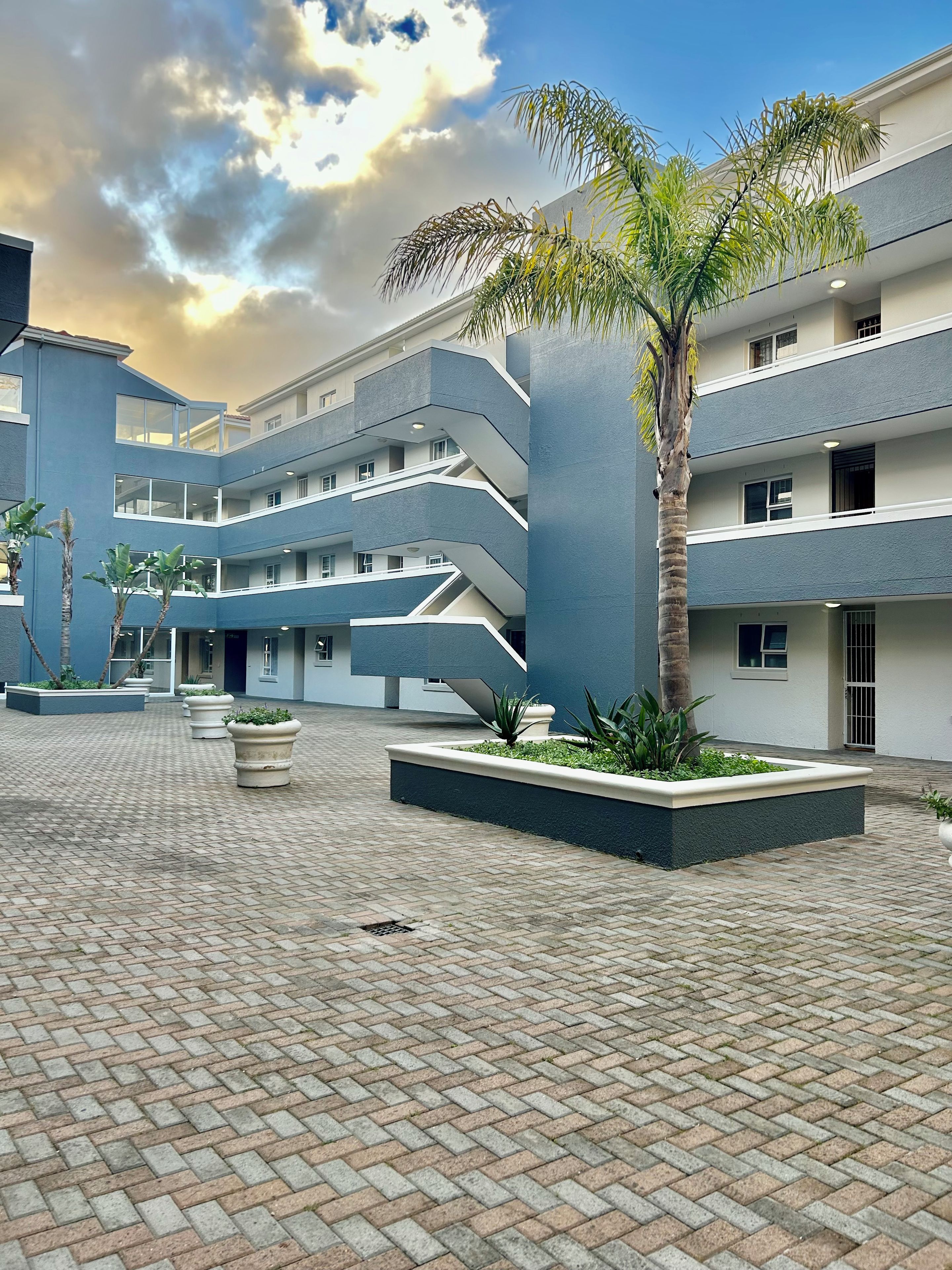 Un edificio de varios pisos con un patio central, una palmera y jardineras.
