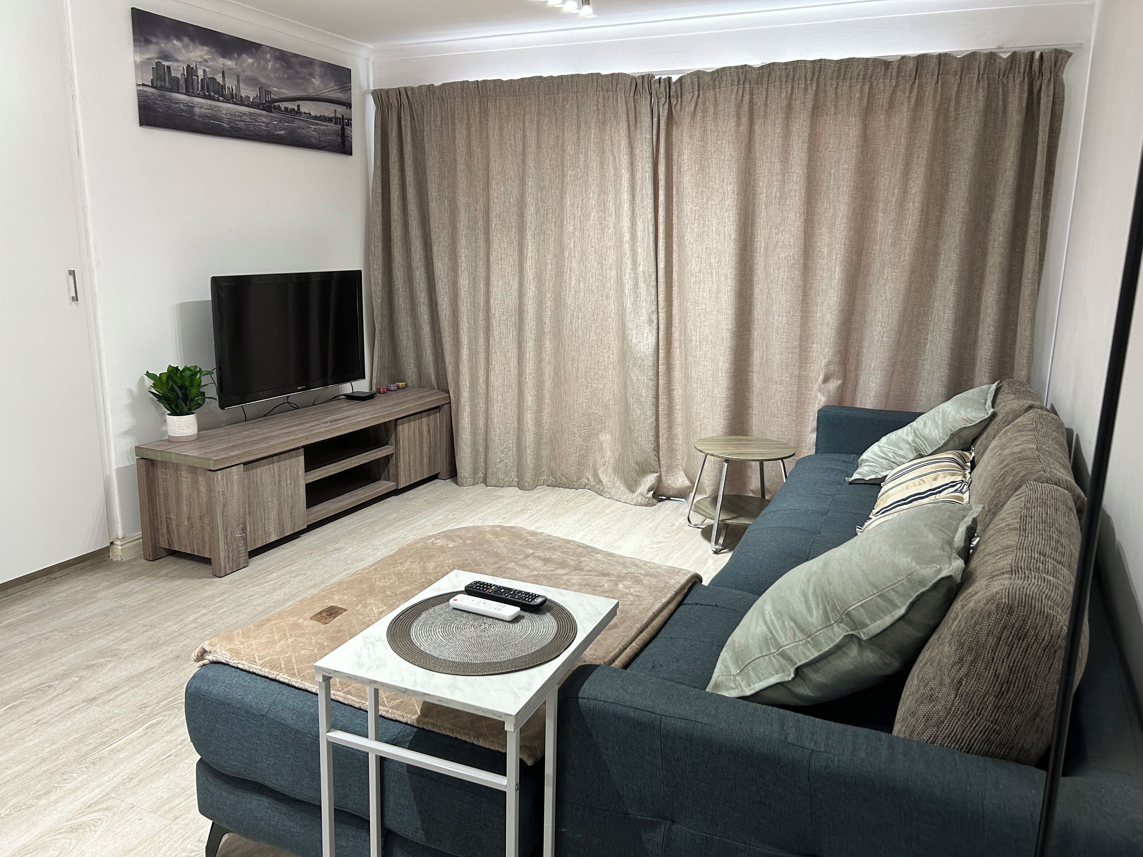 A living room with a sofa, a coffee table, a TV on a wooden stand, and a curtain.