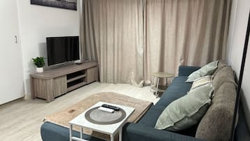 A living room with a sofa, a coffee table, a TV on a wooden stand, and a curtain.