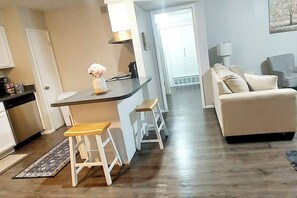 A modern kitchen with a bar area, a dining table with stools, a sofa, and a lamp.