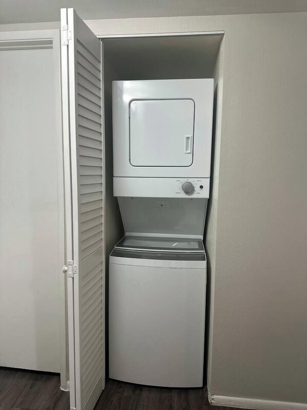 A compact, built-in laundry machine in a corner of a room with a closed door and a white wall.
