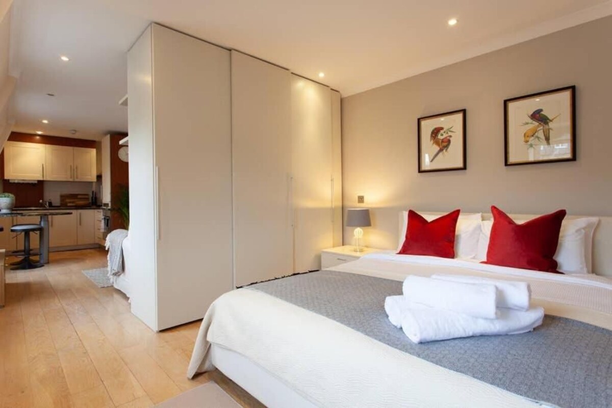 A hotel room with a bed, bedside table, and a view of the kitchen.