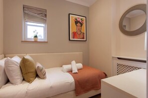 A bedroom with a bed, pillows, a window with a view, a framed picture on the wall, and a mirror. -  Comfortable Apartments in Kensington by Short Stories London (London)