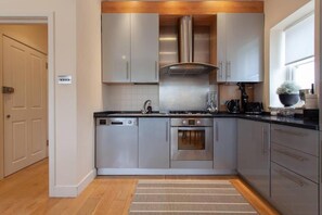 A modern kitchen with stainless steel appliances, a built-in oven, and a range hood. -  Comfortable Apartments in Kensington by Short Stories London (London)