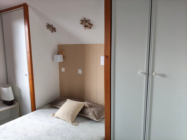Een slaapkamer met een bed, nachtkastje, lamp en een deur.