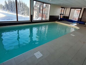 Une piscine intérieure avec de grandes baies vitrées, un sol carrelé et une vue sur un paysage enneigé.