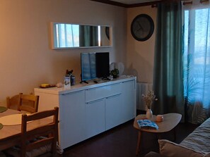 Een woonkamer met een televisie, een klok, een klein tafeltje en een bank.