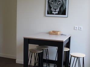 Ein kleiner Tisch mit heller Tischplatte und schwarzen Beinen, begleitet von drei mit heller Sitzfläche ausgestatteten Hocker.