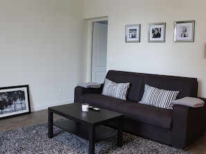 Ein Wohnzimmer mit einem dunkelgrauen Sofa, einem schwarzen Couchtisch und einem gerahmten Bild an der Wand.