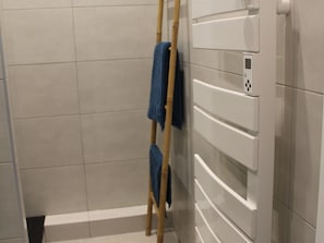 Ein Badezimmer mit Fliesenboden, einer an der Wand lehnten Holzleiter und einem Handtuch, das an der Leiter hängt.