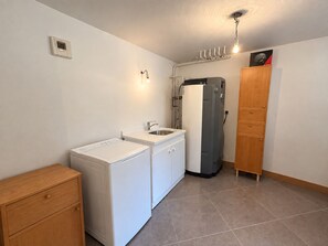 A compact kitchen with a washing machine, a refrigerator, and a wooden cabinet. - Spacious chalet - 8 guests, mountain view (Les Saisies)