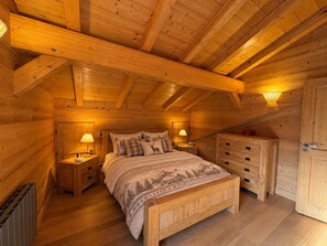 A wooden cabin bedroom with a bed, nightstands, a dresser, and a door. - Spacious chalet - 8 guests, mountain view (Les Saisies)