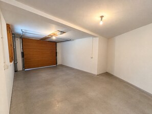 A spacious, empty room with a concrete floor, a wooden door, and a ceiling-mounted light fixture. - Spacious chalet - 8 guests, mountain view (Les Saisies)