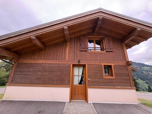 A two-story wooden chalet with a sloped roof, a front door, and a small window. - Spacious chalet - 8 guests, mountain view (Les Saisies)
