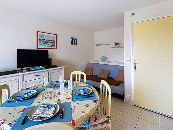 Ein Essbereich mit einem Tisch für zwei Personen, einem Fernseher auf einem Schrank und einer Tür rechts.