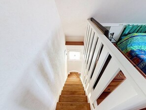 Eine Treppe mit Holzboden und weißen Geländern führt zu einem Schlafzimmer mit einem farbenfrohen Bettüberwurf.