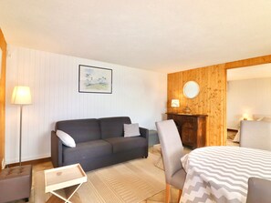 A cozy room with a grey sofa, a wooden cabinet, and a bed with a patterned bedspread. - 50m² apartment, lake view - 2 guests (Veyrier-du-Lac)