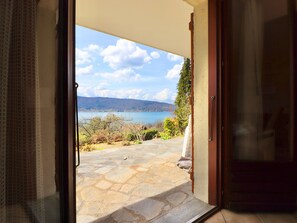 Eine geöffnete Tür führt auf eine Steinterrasse mit Blick auf einen See und Berge.