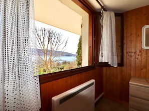 A room with a wooden interior, a radiator, a window with a view of a lake and trees, and a white curtain. - 50m² apartment, lake view - 2 guests (Veyrier-du-Lac)