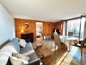 Ein gemütliches Wohnzimmer mit einer Couch, einem Holzespeisetisch mit Stühlen, einem Fernseher und einer kleinen, weißen Kommode.