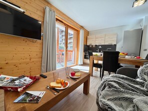 A cozy room with a wooden floor, a dining table with a meal, a TV, and a view of a balcony. - Modern apartment - 4 guests (Vars)