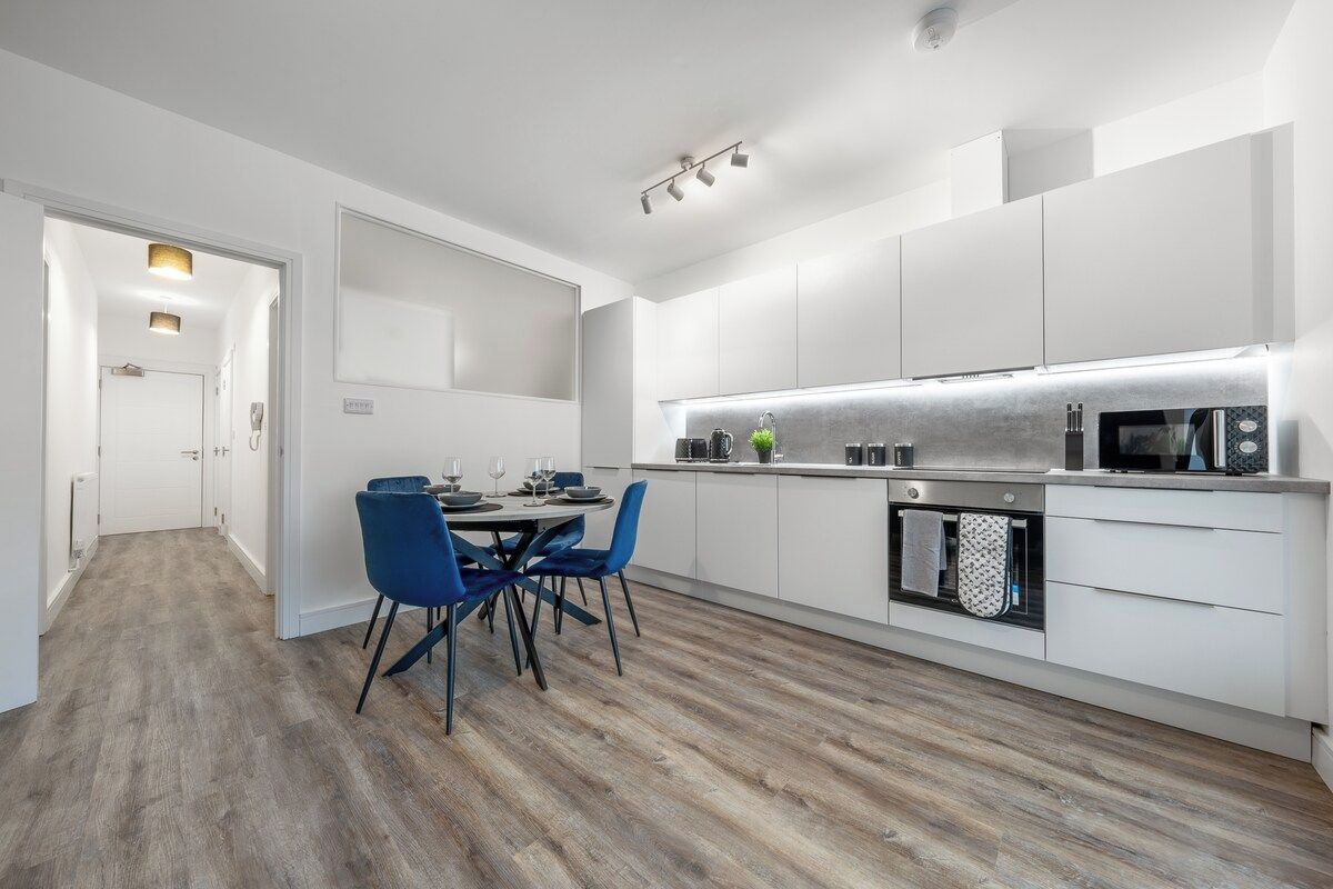 A modern kitchen with white cabinetry, a dining area with blue chairs, and a wooden floor.