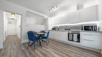 A modern kitchen with white cabinetry, a dining area with blue chairs, and a wooden floor.