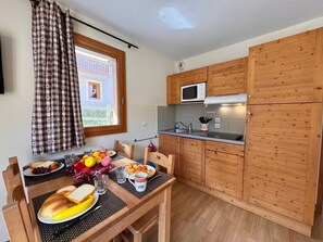 A compact kitchen with wooden cabinets, a microwave, and a dining table set with food and drinks. - Apartment mountain view - 4 guests (Vars)