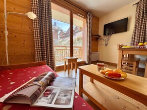 Une pièce confortable avec un lit, une table sur laquelle se trouve une assiette de fruits, un magazine et une fenêtre avec des rideaux.
