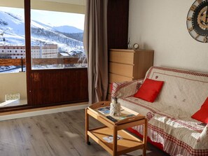 A cozy living room with a wooden floor, a sofa with a checkered cover, a small table with a vase, and a view of a snowy landscape through a window. - Bright studio - 4 guests, near ski lift (Saint-François-Longchamp)