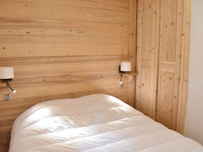 Une pièce aux murs lambrissés, comprenant un lit, deux lampes fixées au mur et une porte.