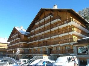 Ein mehrstöckiges Holzgebäude mit Balkonen, vermutlich ein Hotel oder eine Pension, mit parkenden Autos davor.
