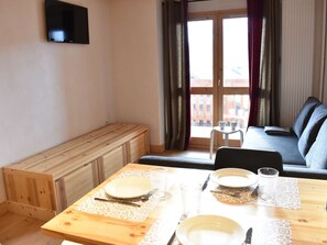 A dining area with a wooden table set for two, a bench, and a sofa in the background. - Apartment with mountain view - 4 guests (Méribel)
