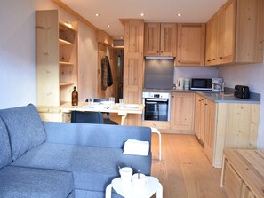 Ein kompakter Wohnbereich mit Küchenzeile, Essbereich und Sitzecke mit Sofa und kleinem Tisch.