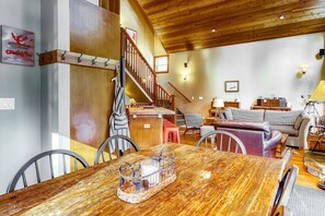 A cozy living room with a wooden dining table, a sofa, and a staircase leading to an upper level. - Beautiful 3BR Lakeview | 2 Living Rooms | Hot Tub (Soda Springs)