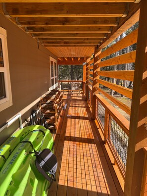 A wooden deck with kayaks and a paddleboard, leading to a covered area with a view of trees. - Beautiful 3BR Lakeview | 2 Living Rooms | Hot Tub (Soda Springs)