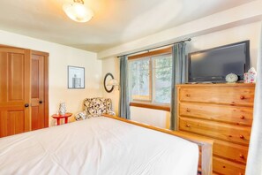 Habitación de hotel con una cama, cómoda de madera, televisor, reloj y ventana con cortinas.