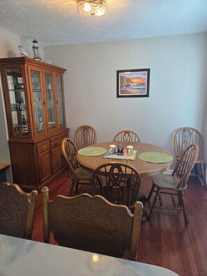 Un comedor con mesa de madera, sillas, un armario con puertas de vidrio y un cuadro en la pared.