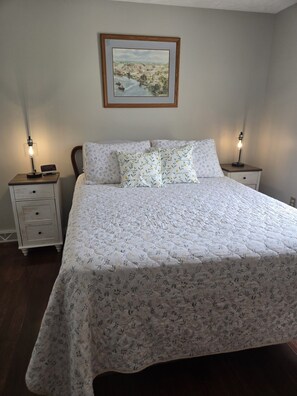 Une chambre à coucher avec un lit, deux tables de chevet, une commode, un tableau encadré au mur et une horloge sur la commode.