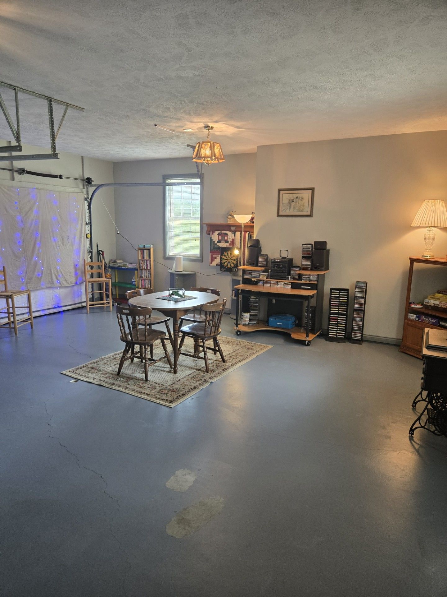 Una habitación con una mesa redonda, sillas, un ventilador de techo, una estantería, una lámpara y una ventana con persianas.