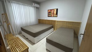 Habitació amb dos llits, una escala de fusta, un cortinatge blanc i un aire condicionat fixat a la paret.