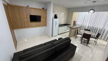 Cozinha moderna com televisão integrada, geladeira e área de jantar com mesa e cadeiras.