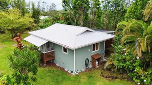 A single-story house with a gabled roof, surrounded by lush greenery and trees. - Nani Mala Cove at Island Rainforest Grove (Keaau)